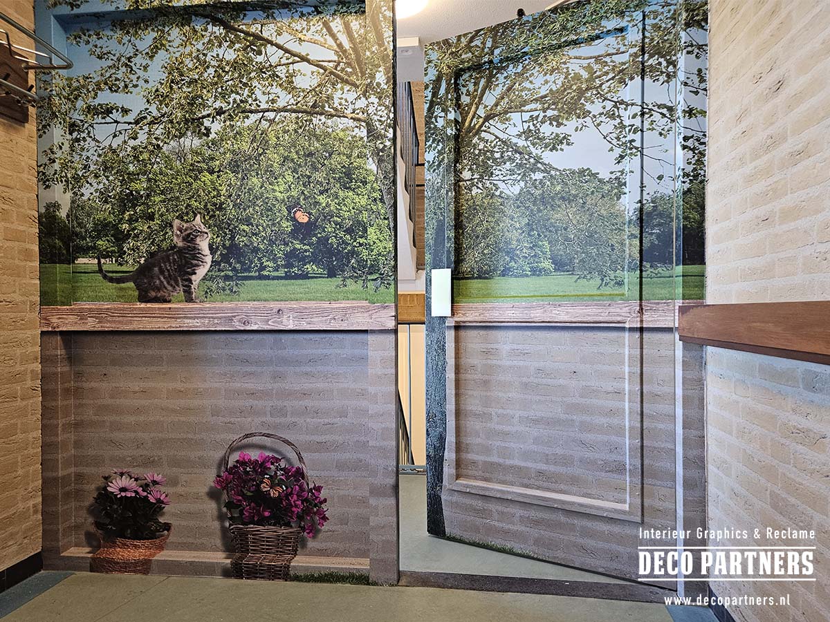 Dementievriendelijk ontwerp waarmee een deur en toegang tot een trappenhuis visueel worden gecamoufleerd als een sfeervolle tuinmuur met uitzicht op een park. Leuk detail zijn de poes en de vlinder op het muurtje.