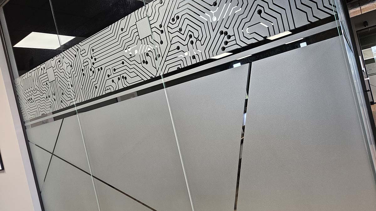 Detail van matglasfolie met een uitgesneden patroon van elektronische verbindingen op een glazen kantoorwand.