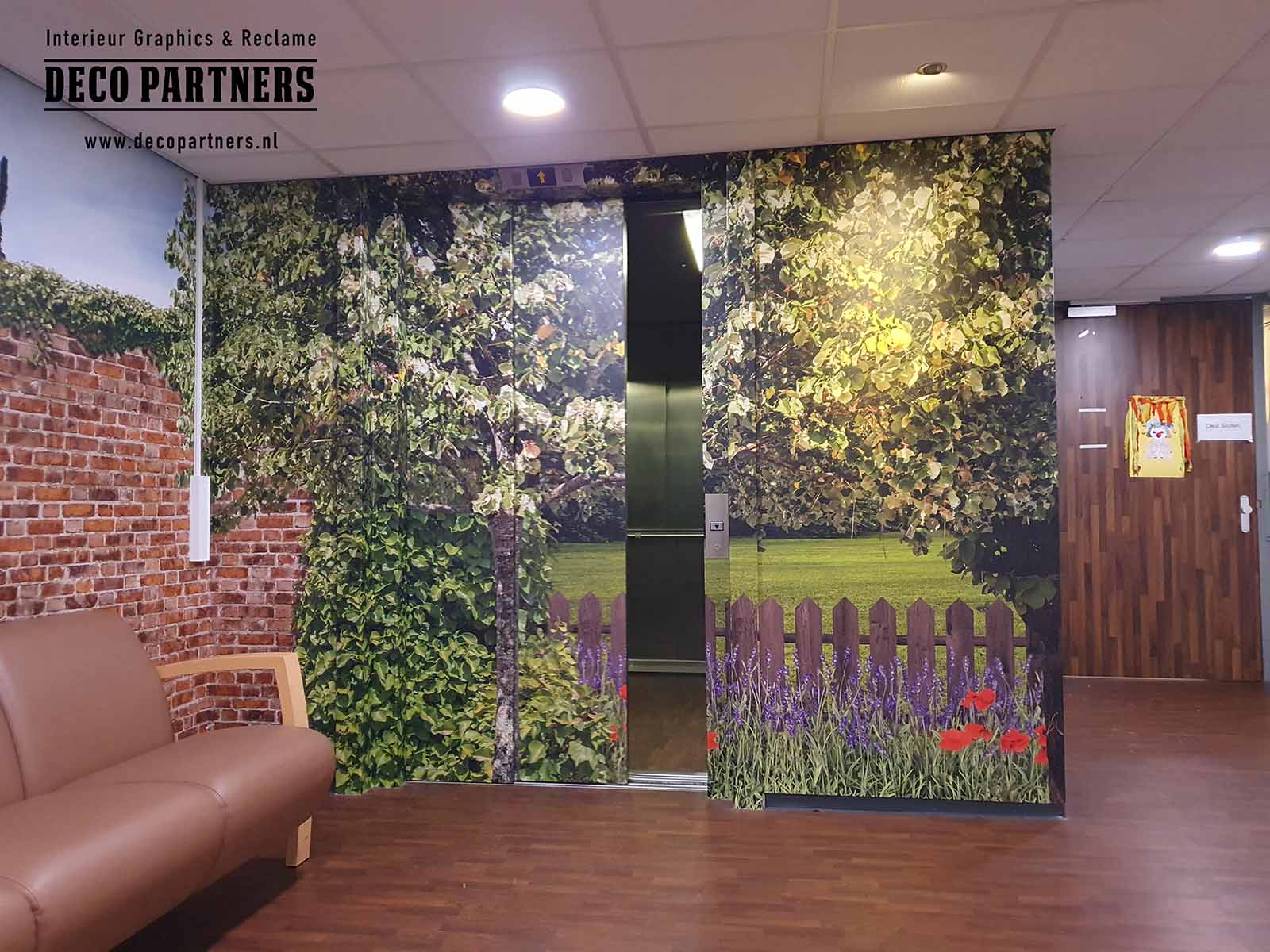 Liftdeuren in een zorginstelling voorzien van een rustgevende natuurprint met bomen, groen en bloemen. Door het ontwerp lijkt de lift onderdeel van de wand en valt deze minder op in de ruimte. Deze vorm van liftwrapping wordt toegepast om een rustige en huiselijke uitstraling te creëren en om de lift visueel te laten opgaan in de omgeving, wat kan bijdragen aan het verminderen van onrust en dwaalgedrag bij dementerende bewoners.