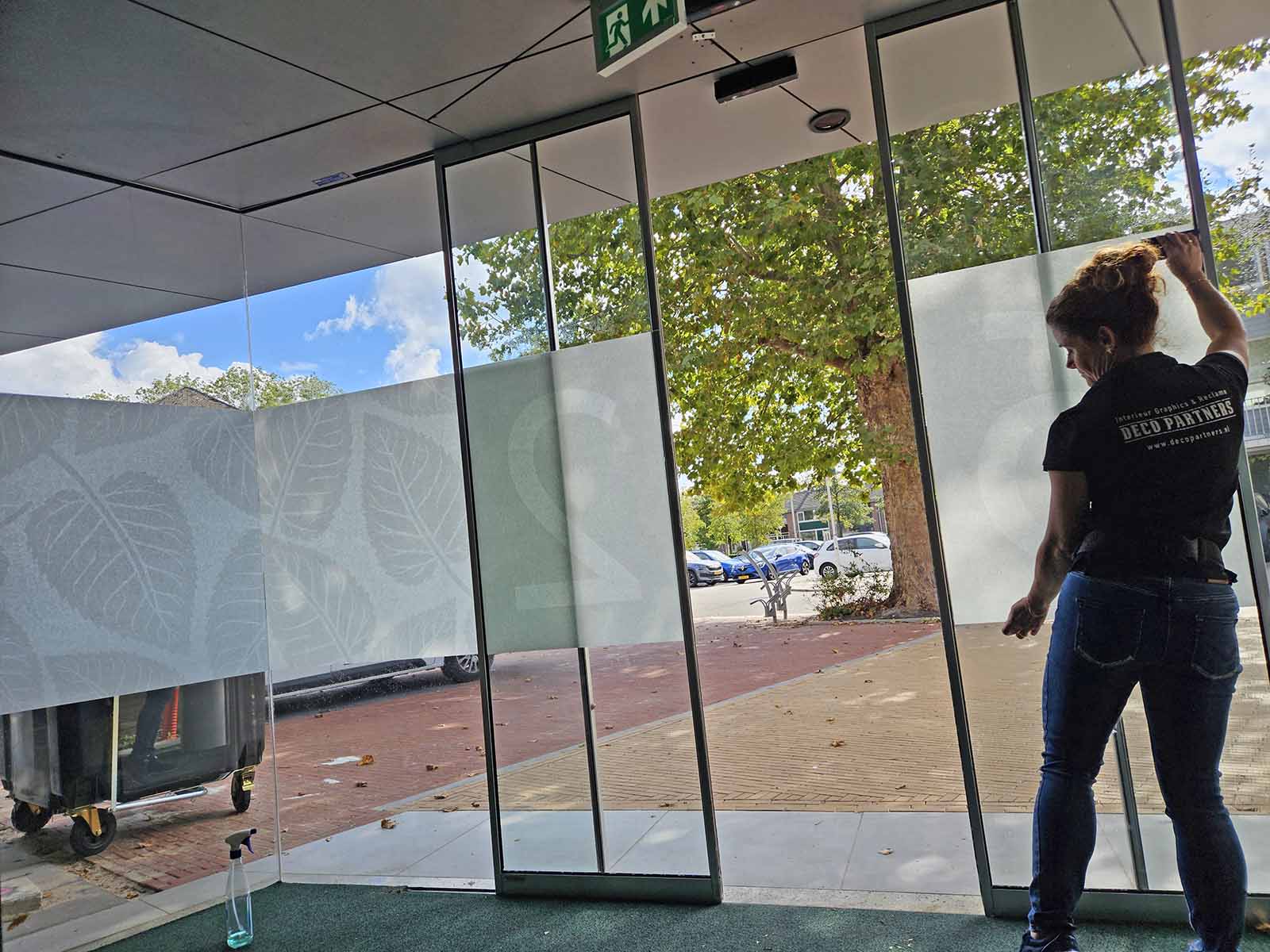 Vakkundige montage van matglasfolie met bladerenpatroon en huisnummer door DecoPartners