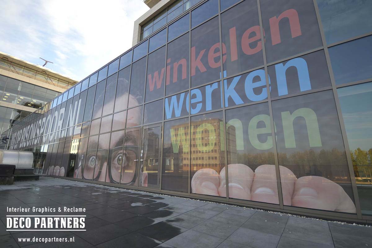 XXL One Way Vision raamfolie met groot reclamebeeld over meerdere raampartijen van een glazen gevel.