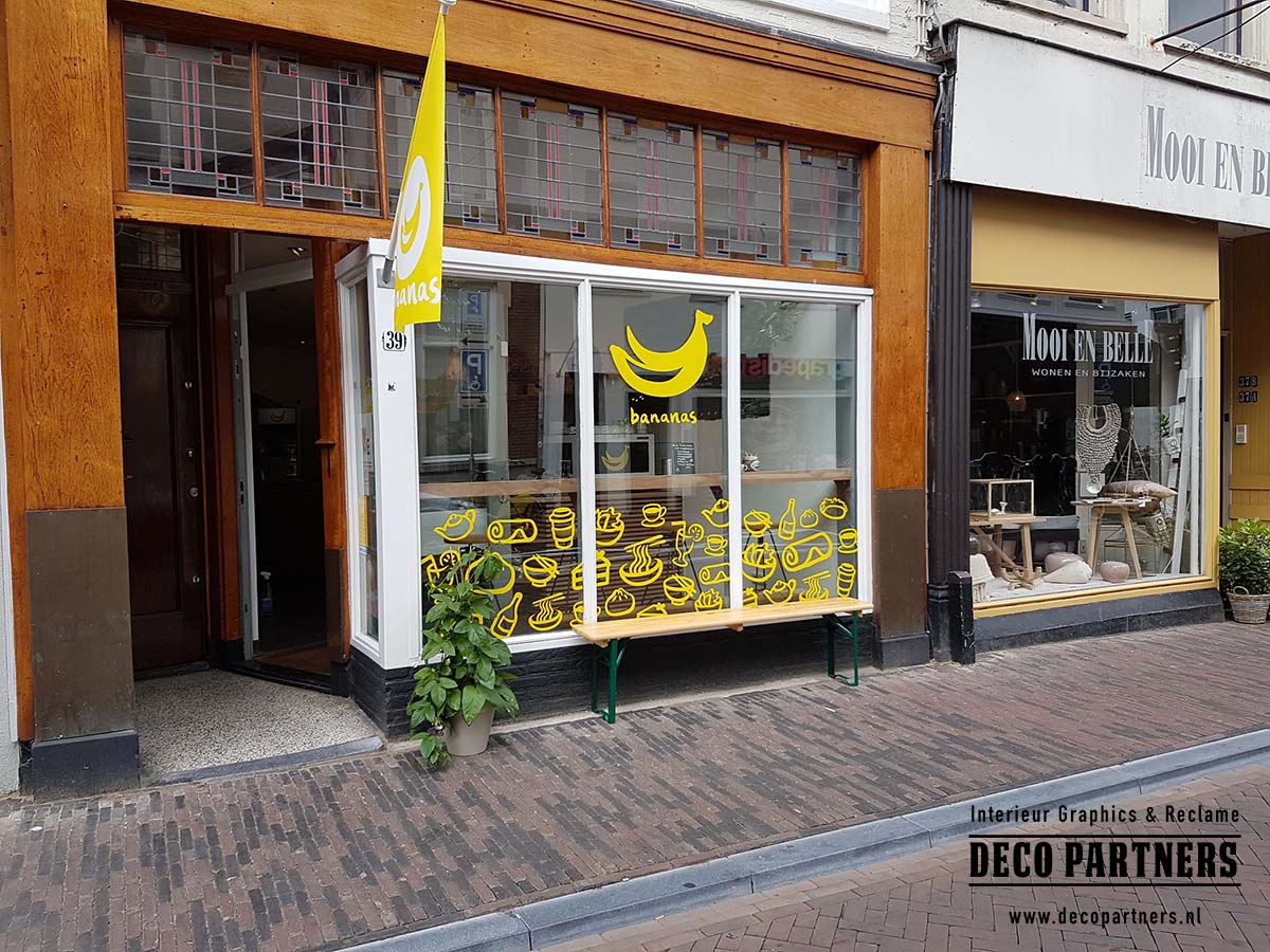 Raambelettering op maat voor winkel en etalage Raambelettering op winkelruit met logo en uitgesneden illustraties