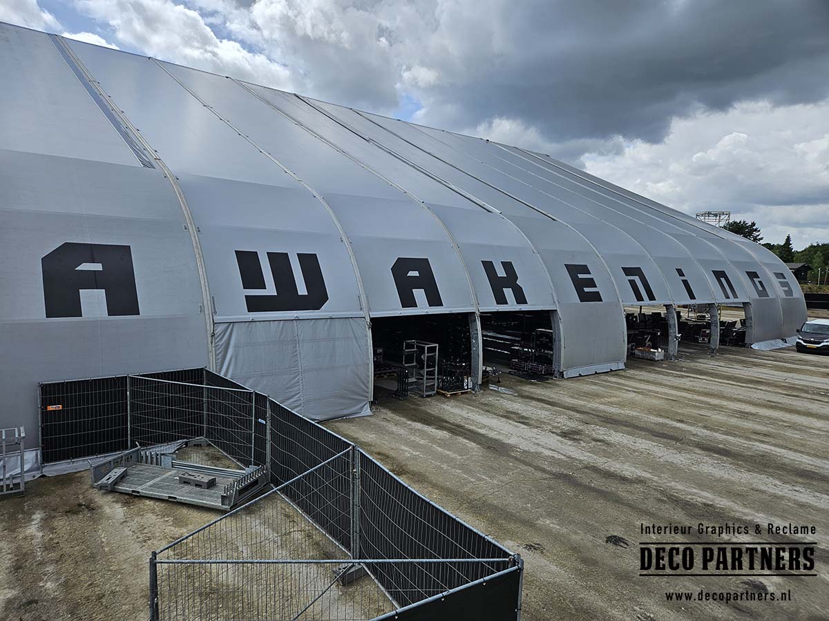 Grote tijdelijke bestickering met zwarte letters op een evenementenconstructie tijdens een festival.