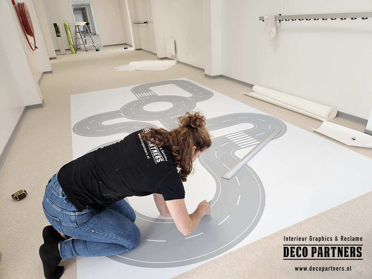 Monteur brengt een verwijderbare autobaan als vloerbestickering aan in een tijdelijke kinderopvang in een noodgebouw.